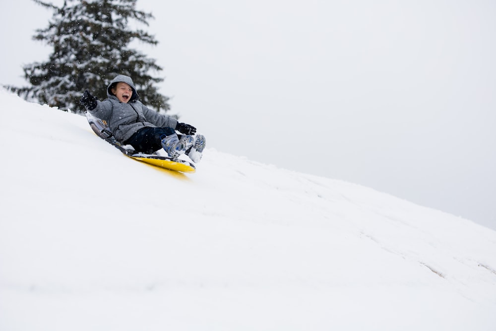 hombre con chaqueta negra montando trineo de nieve amarillo en terreno cubierto de nieve durante el día