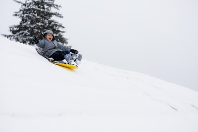 man in black jacket riding yellow snow sled on snow covered ground during daytime sled zoom background