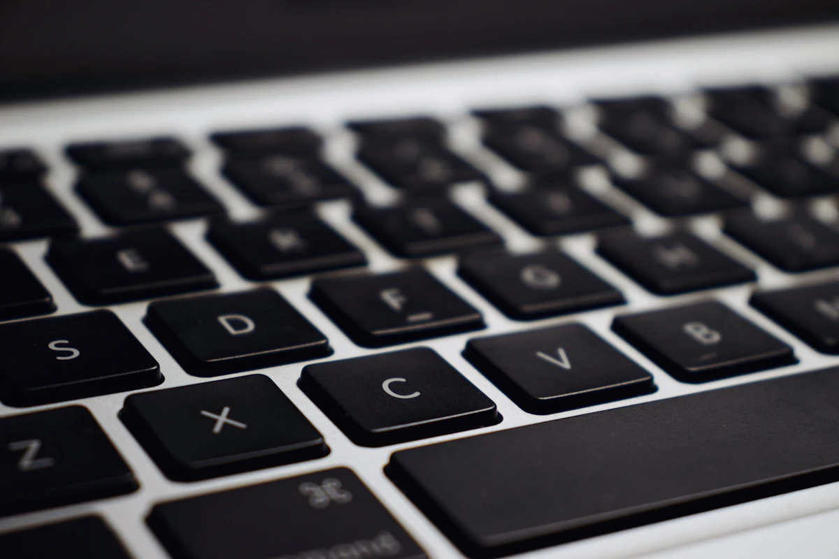 Laptop hitam silver di atas meja sebagai ilustrasi proses mengelap permukaan keyboard dengan kain microfiber lembap berisi isopropil alkohol untuk menghilangkan minyak dan kuman