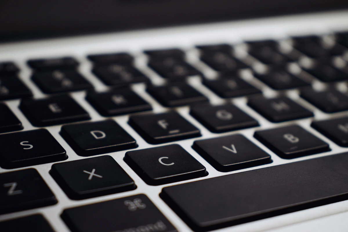Laptop hitam silver di atas meja sebagai ilustrasi proses mengelap permukaan keyboard dengan kain microfiber lembap berisi isopropil alkohol untuk menghilangkan minyak dan kuman