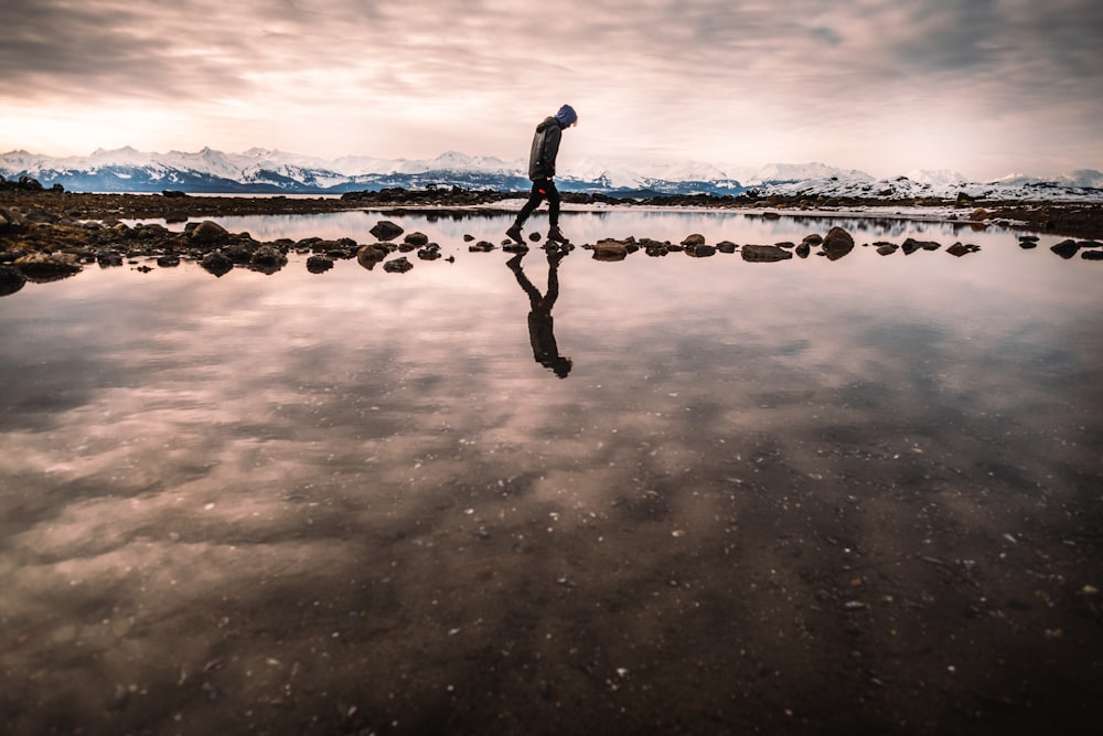 silhouette of man standing on seashore during sunset