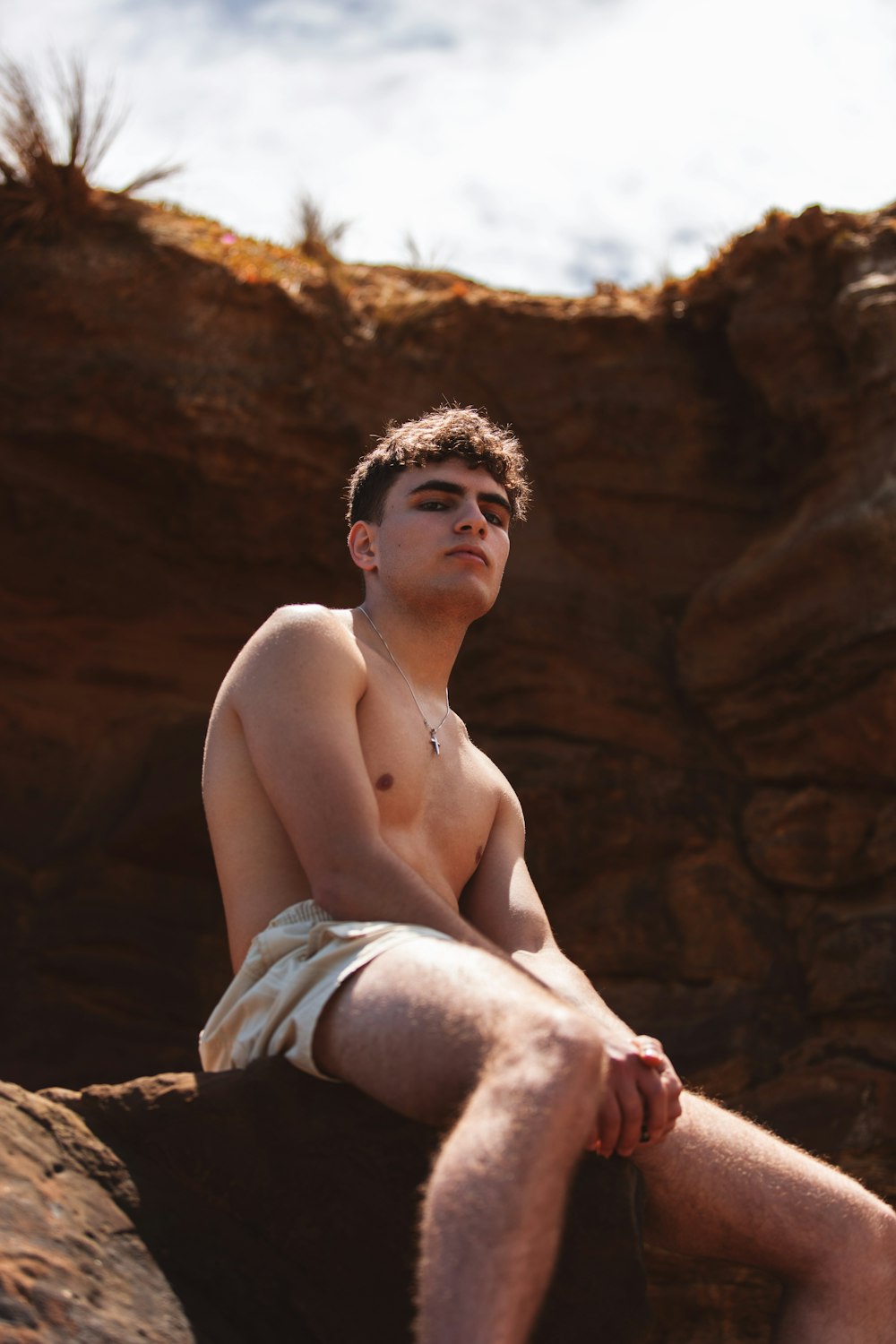 topless man in white shorts sitting on brown rock