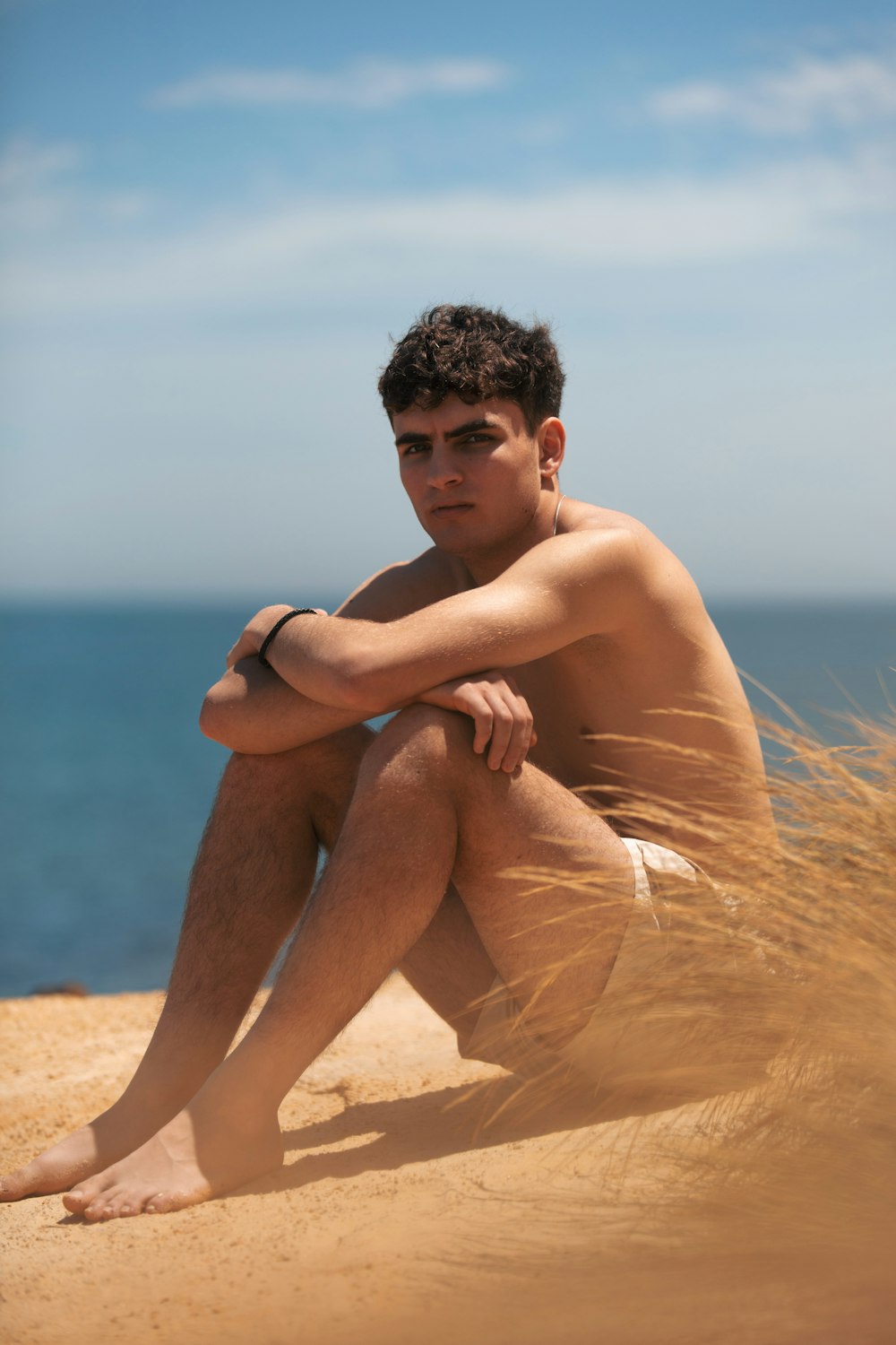 topless man sitting on brown sand during daytime