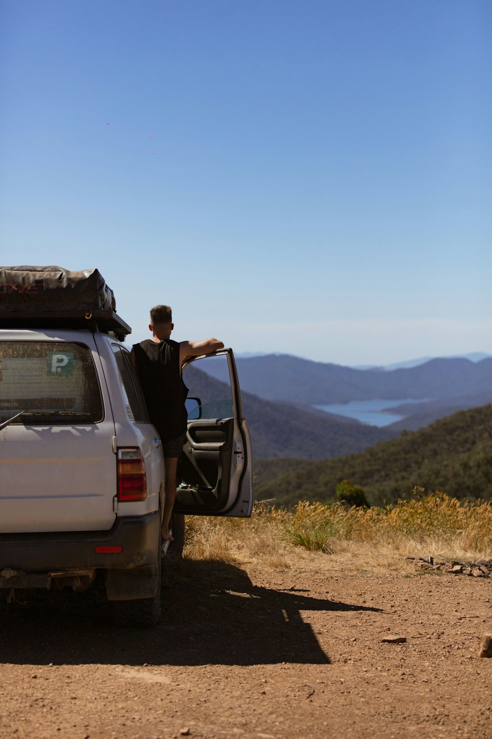 man in black jacket sitting on white suv during daytime