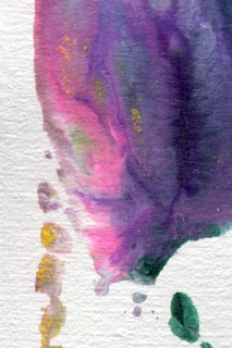A watercolor painting with an abstract design featuring flowing gradients of purple, pink, and hints of yellow. The texture is visible, and the colors blend into each other creating a calming effect. There are small splashes of green and yellow towards the edges.