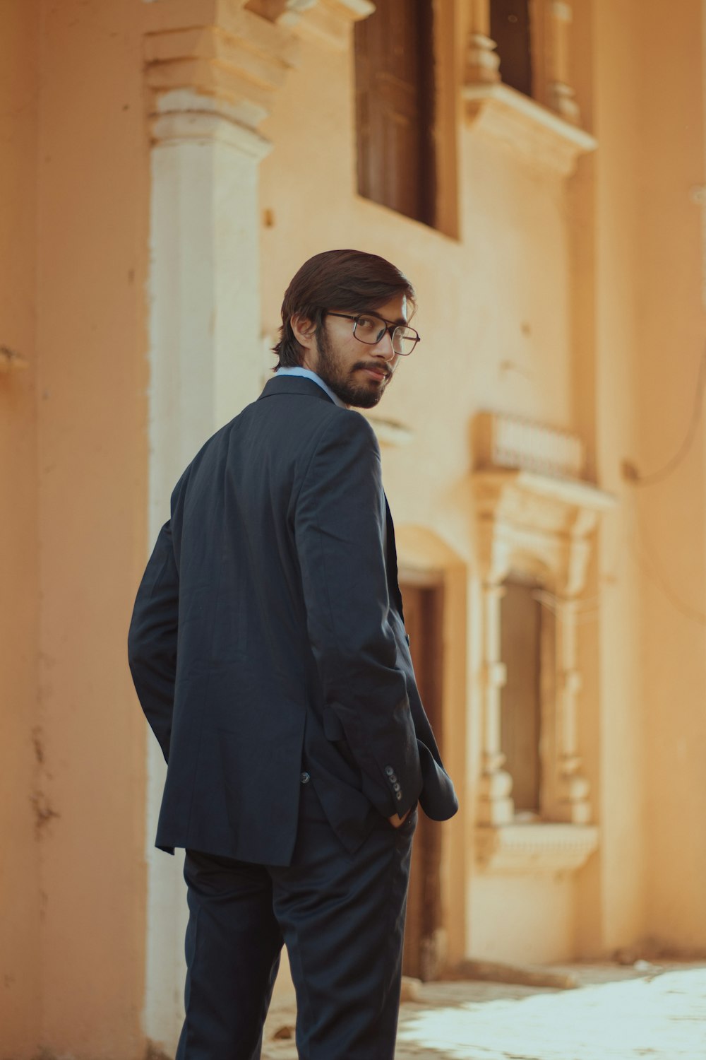 a man in a suit and glasses standing in front of a building