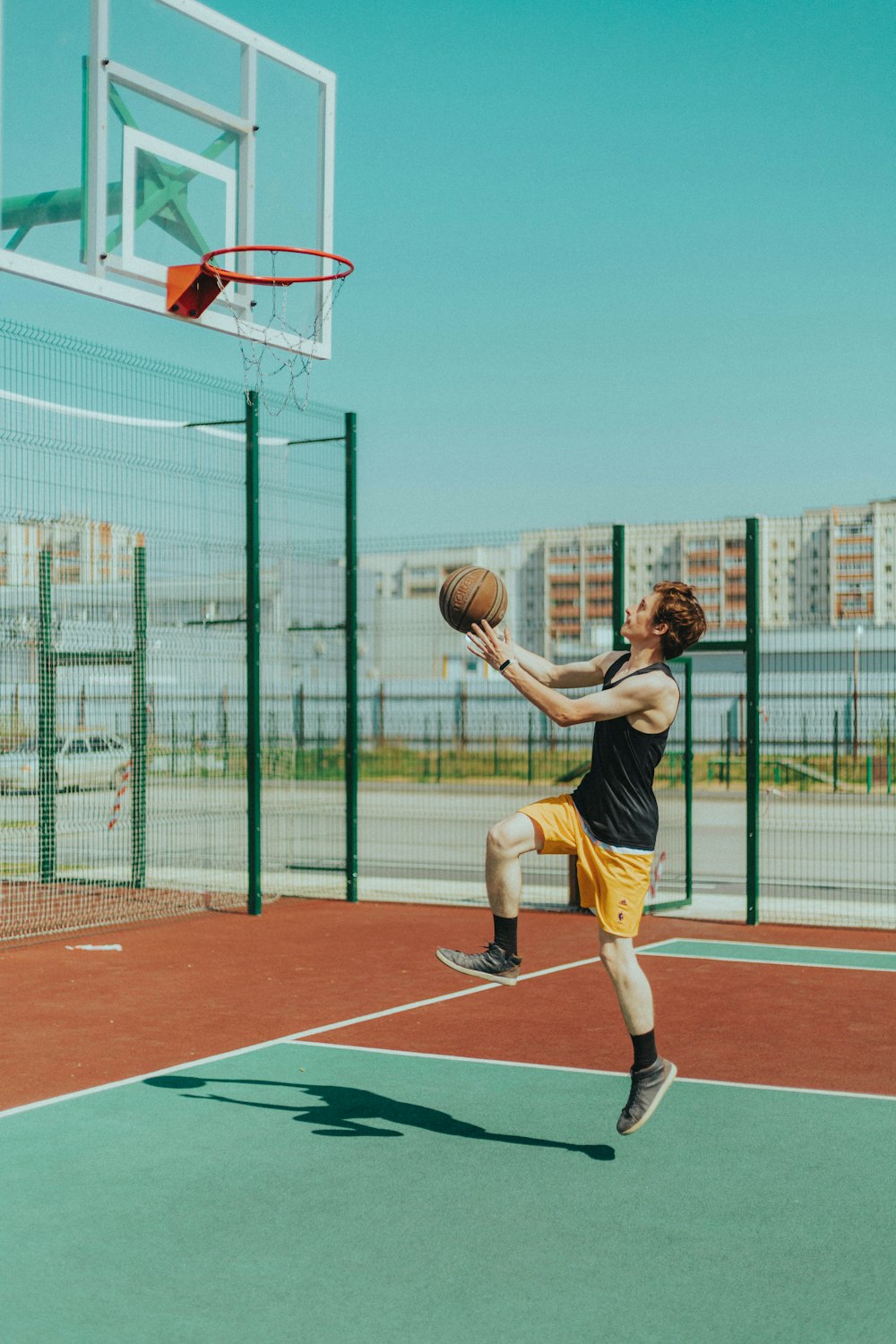 homme en débardeur noir et short jaune jouant au basket-ball pendant la journée