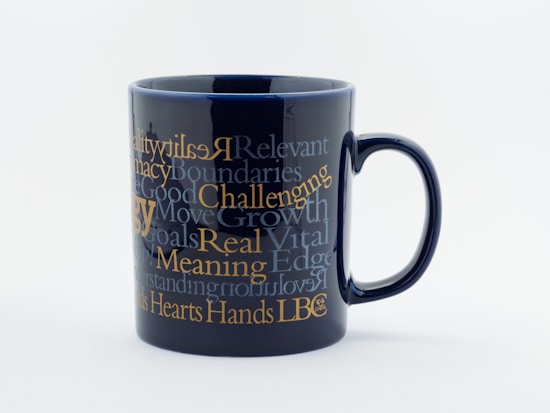 A black ceramic mug adorned with multiple motivational words and phrases in various fonts and sizes. The text is primarily in shades of white and gold, creating a striking contrast against the dark background.
