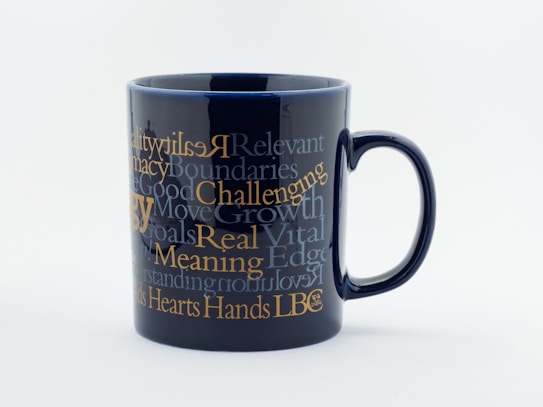A black ceramic mug adorned with multiple motivational words and phrases in various fonts and sizes. The text is primarily in shades of white and gold, creating a striking contrast against the dark background.