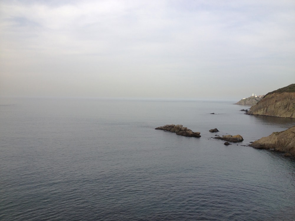 formação rochosa cinzenta no mar sob o céu branco durante o dia