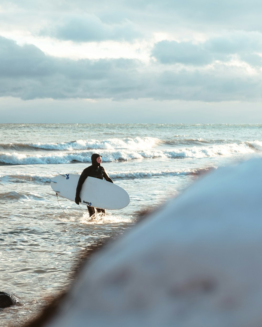 woman in black tank top and white pants carrying white surfboard walking on beach during daytime