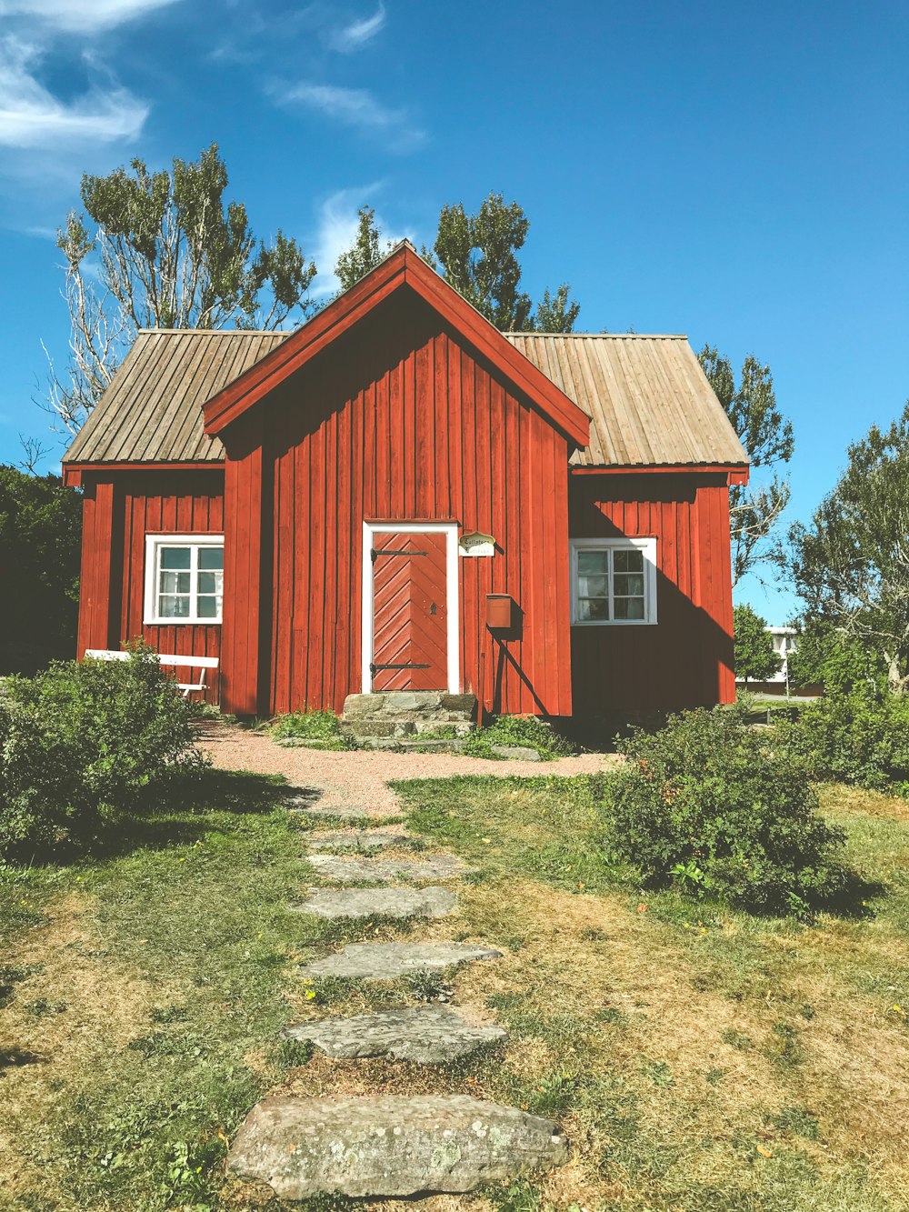 red and white wooden house near green trees under blue sky during daytime