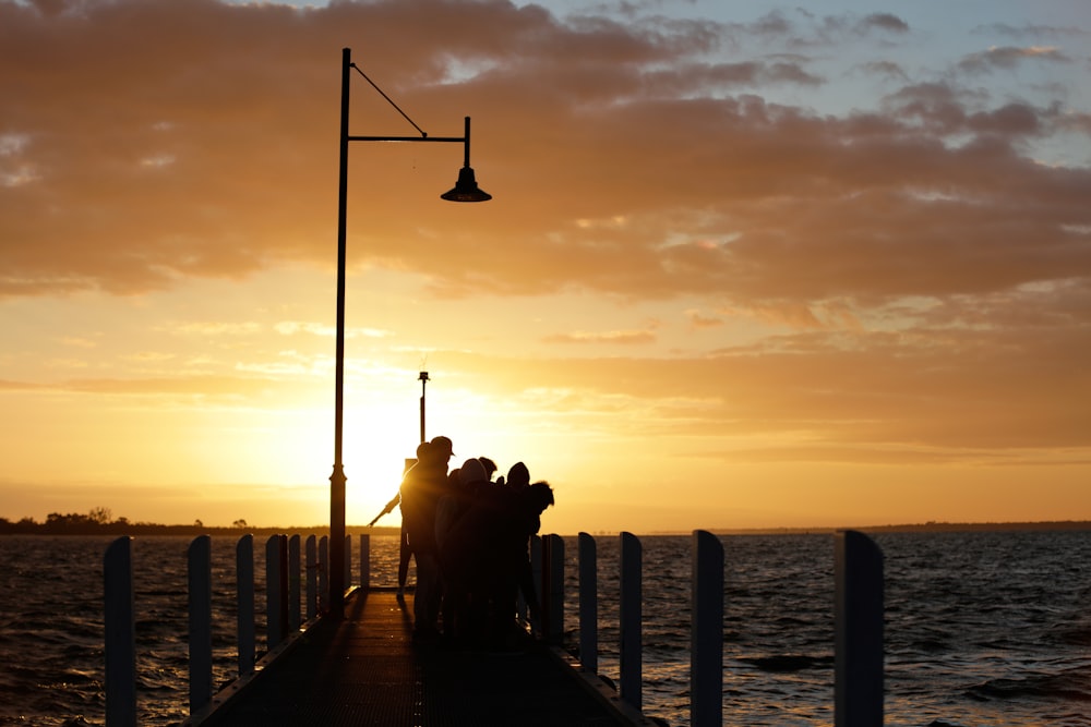 silhouette of people on dock during sunset