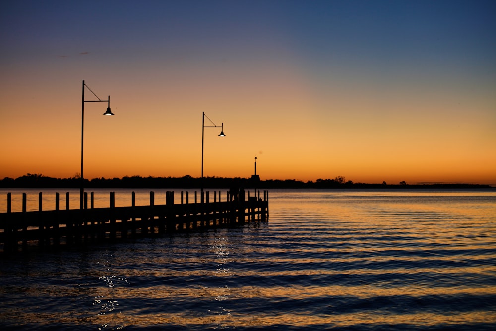 silhouette of wooden dock on sea during sunset