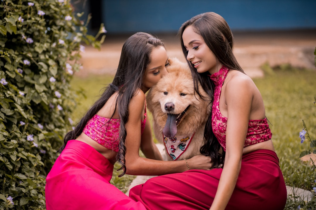 woman in pink tank top and red pants sitting beside brown dog