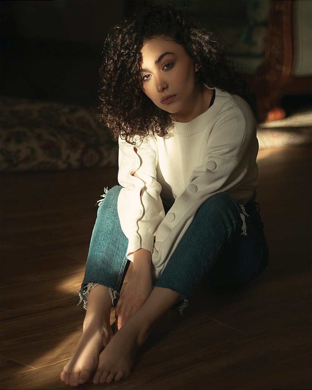 girl in white long sleeve shirt and blue denim jeans sitting on brown wooden floor