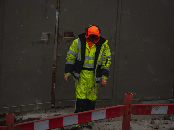 man in green jacket and orange helmet standing on gray concrete floor