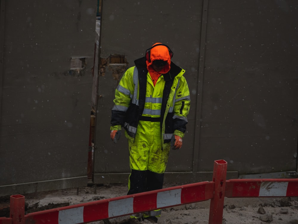 uomo in giacca verde e casco arancione in piedi sul pavimento di cemento grigio