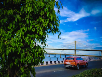 orange car on gray concrete road near bridge under blue sky during daytime
