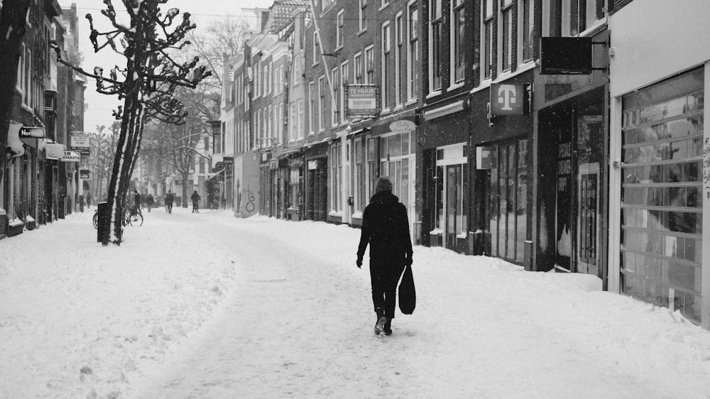 昼間、建物近くの雪に覆われた道路を歩く黒いコートを着た人