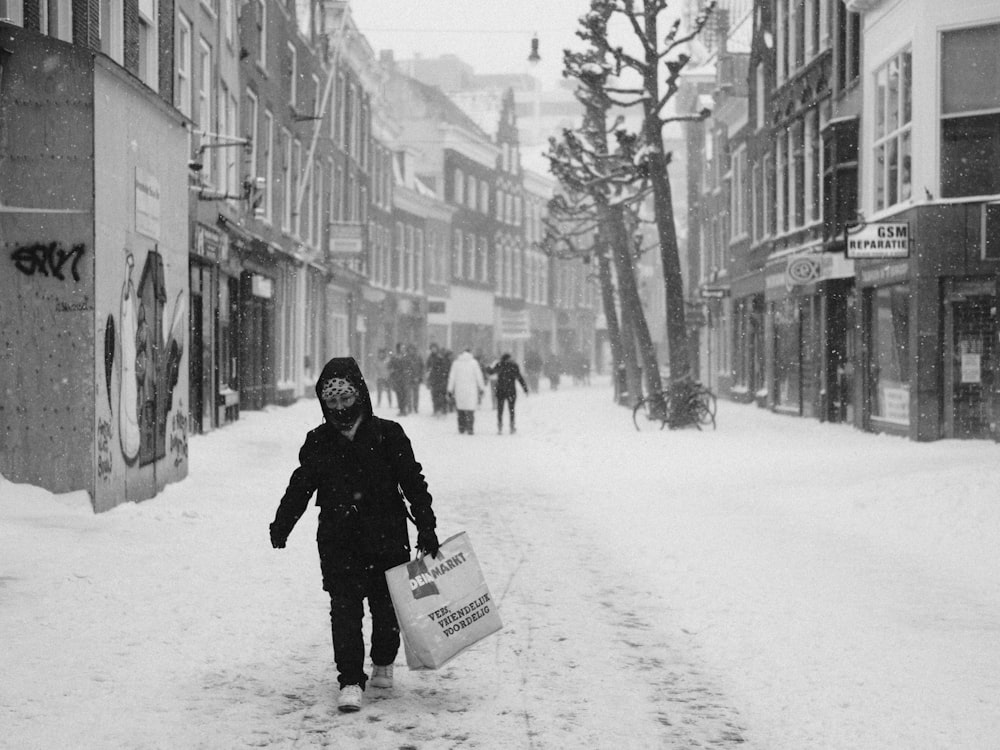 woman in black coat carrying white plastic bag walking on snow covered road