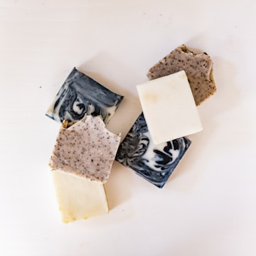 A collection of various handmade soap bars with different textures and colors, including marbled black and white, speckled, and plain white soaps, arranged on a white surface.