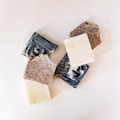 A collection of various handmade soap bars with different textures and colors, including marbled black and white, speckled, and plain white soaps, arranged on a white surface.
