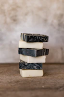 Stacked artisanal soaps with unique fragrance swirls in earthy tones against a sage green background.