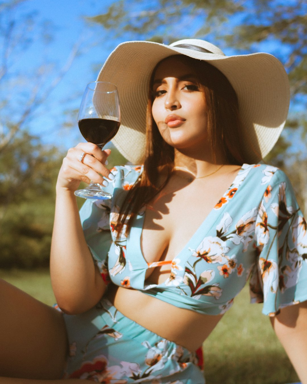 woman in white blue and red floral shirt and white sun hat holding wine glass