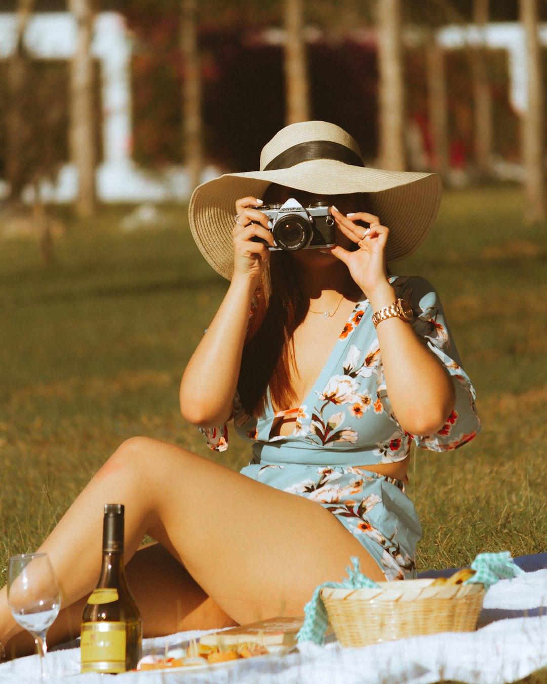 woman in white blue and red floral dress wearing brown hat sitting on green grass field