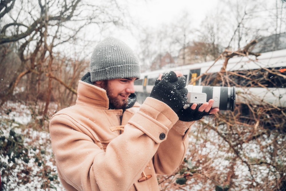 man in brown coat holding black dslr camera