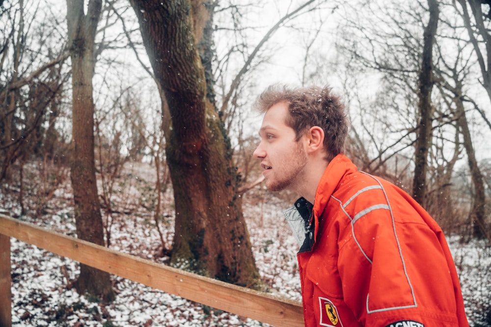 man in orange and black jacket standing near brown wooden fence during daytime