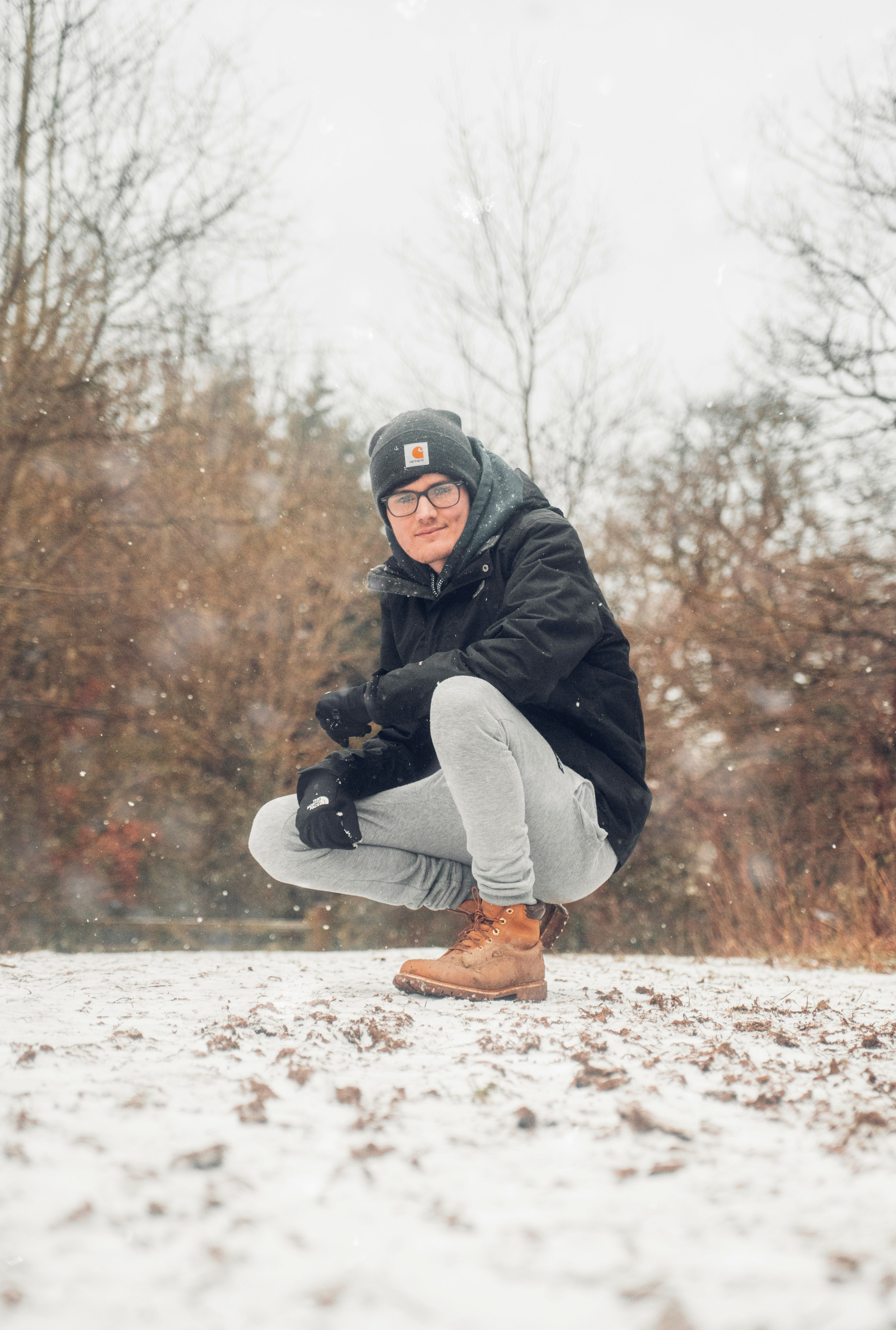 man in black jacket and gray pants sitting on snow covered ground during daytime