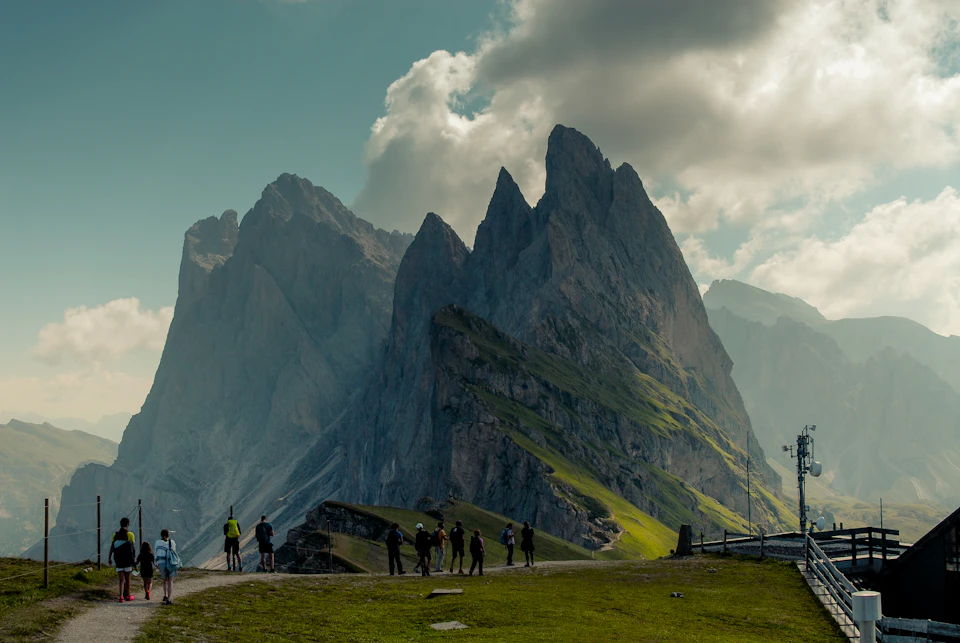 Group of people standing on a grassy hill overlooking majestic mountain range with three peaks