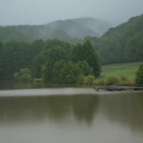 A serene lake reflecting the lush green hills of Dalhousie on a misty morning.