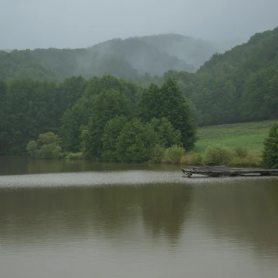 A serene lake reflecting the lush green hills of Dalhousie on a misty morning.