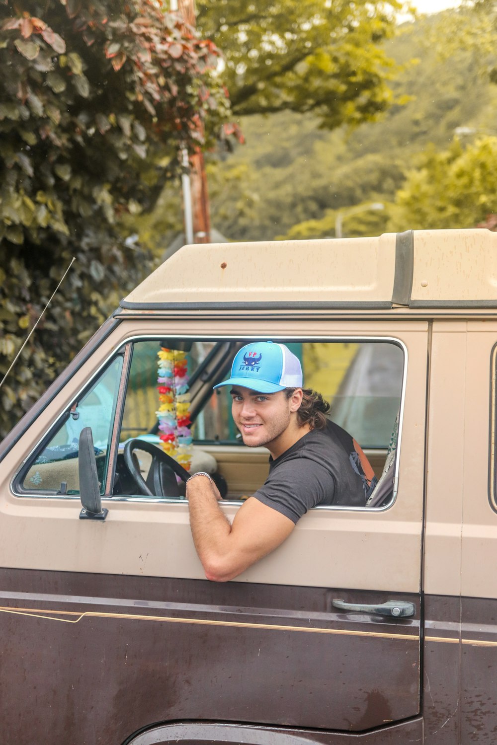 man in black t-shirt and blue cap sitting on white van during daytime