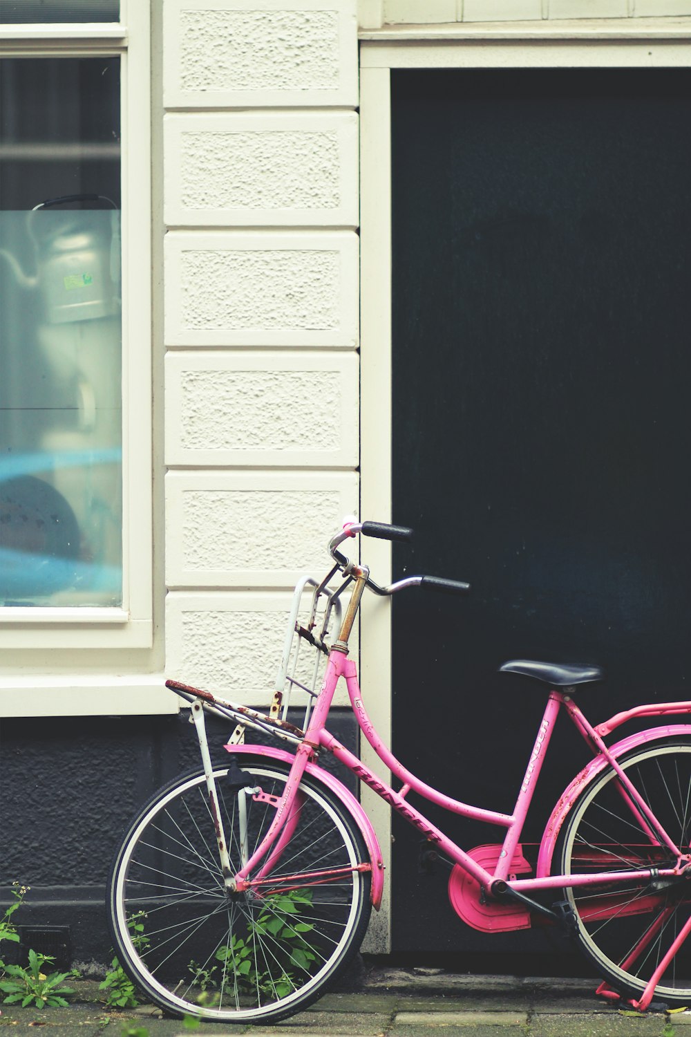 purple city bike parked beside white wooden window