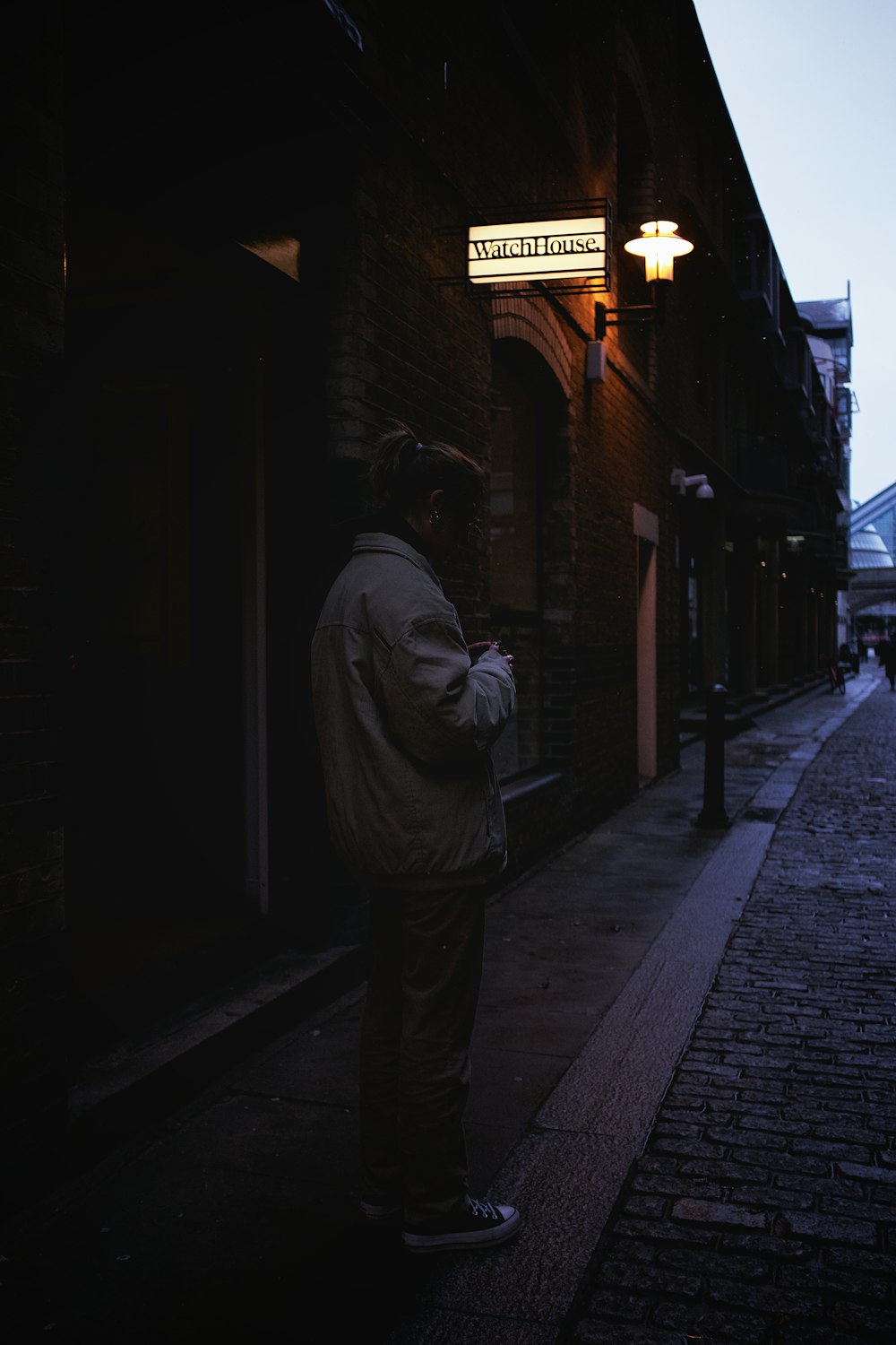 man in gray jacket standing on sidewalk during night time