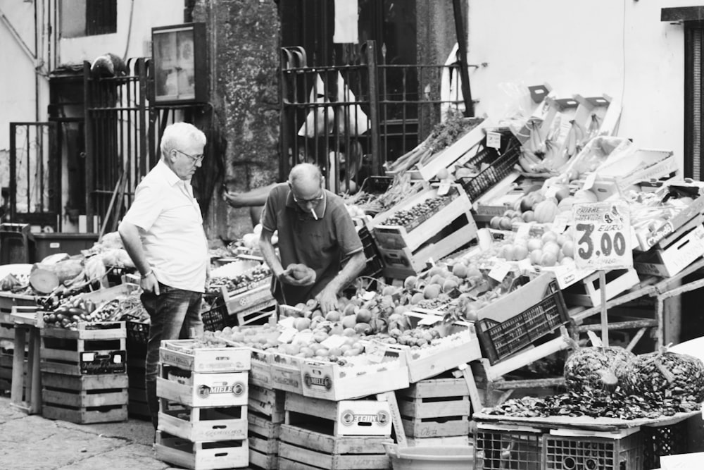 grayscale photo of man in white shirt standing in front of vegetable display