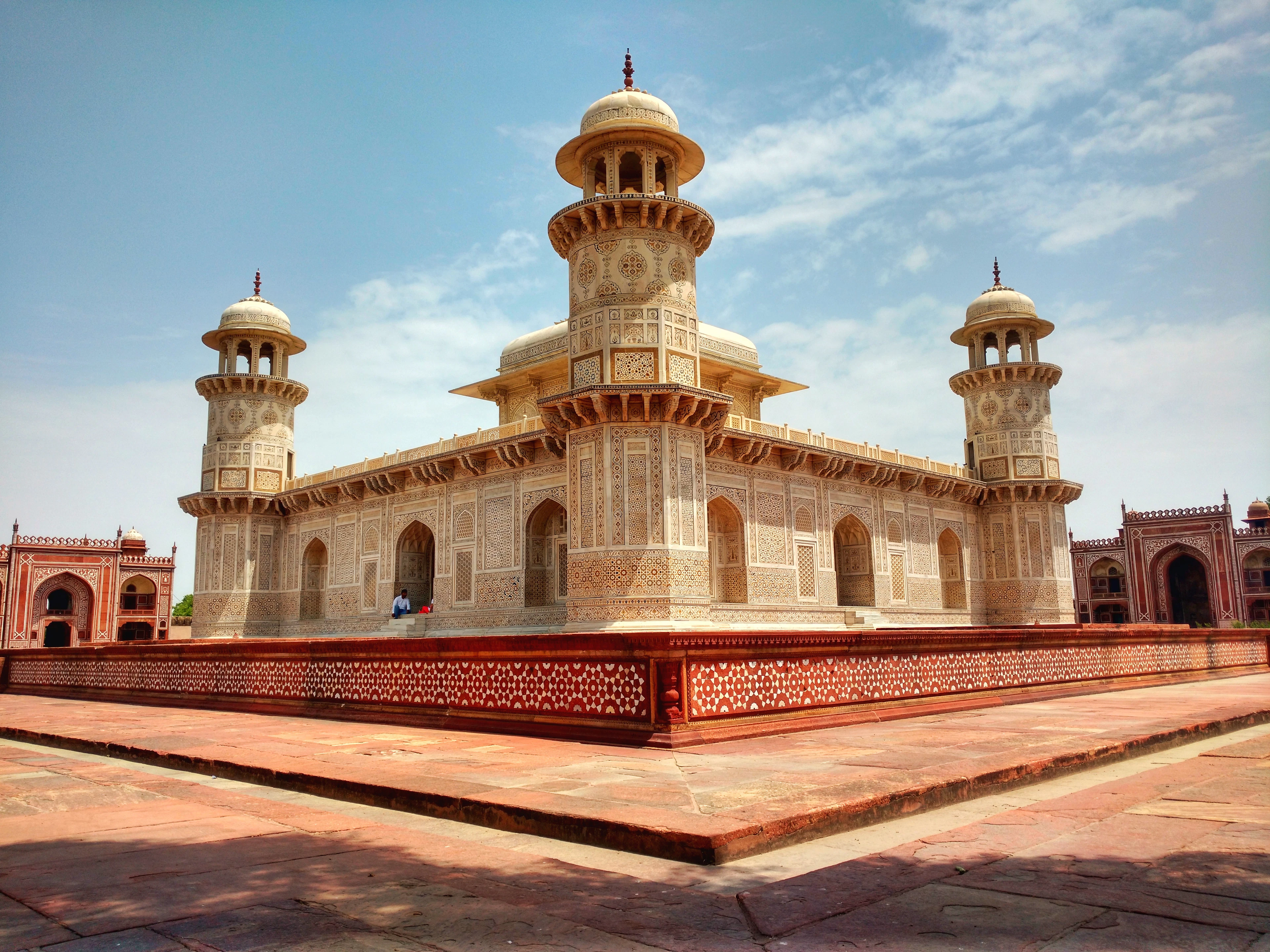 The Tomb of I'timad-ud-Daulah in Agra, the marble 'Baby Taj', its four slender corner minarets and inlaid facade rising from a red sandstone platform under a bright sky.