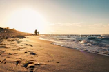 Golden hour light casting long shadows over a quiet beach with gentle waves.
