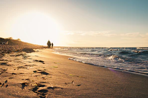 Golden hour light casting long shadows over a quiet beach with gentle waves.