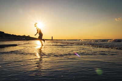 man in white shirt and black shorts jumping on beach during sunset