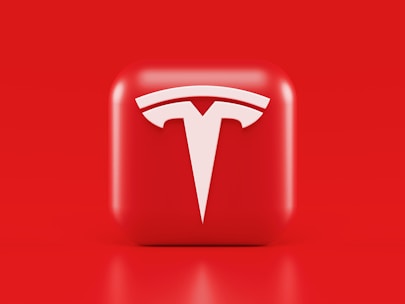 A glossy, red 3D square icon features a white, stylized 'T' logo with a futuristic and sleek design. The background is also solid red, creating a visually striking contrast.