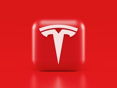 A glossy, red 3D square icon features a white, stylized 'T' logo with a futuristic and sleek design. The background is also solid red, creating a visually striking contrast.