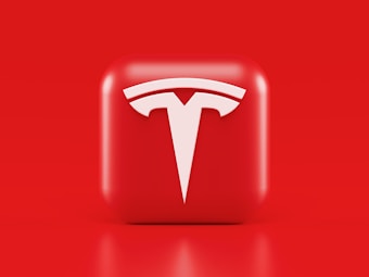 A glossy, red 3D square icon features a white, stylized 'T' logo with a futuristic and sleek design. The background is also solid red, creating a visually striking contrast.