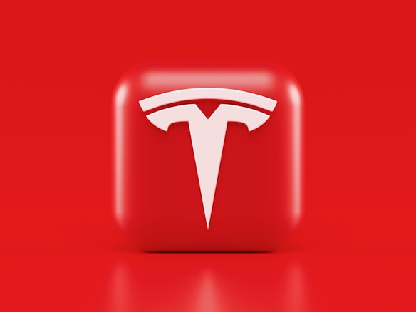 A glossy, red 3D square icon features a white, stylized 'T' logo with a futuristic and sleek design. The background is also solid red, creating a visually striking contrast.