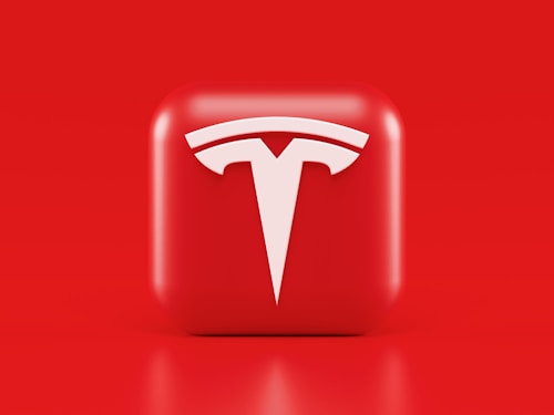 A glossy, red 3D square icon features a white, stylized 'T' logo with a futuristic and sleek design. The background is also solid red, creating a visually striking contrast.