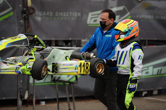 Savannah Maddox in her racing suit, helmet in hand, standing beside her kart on a sunny track.
